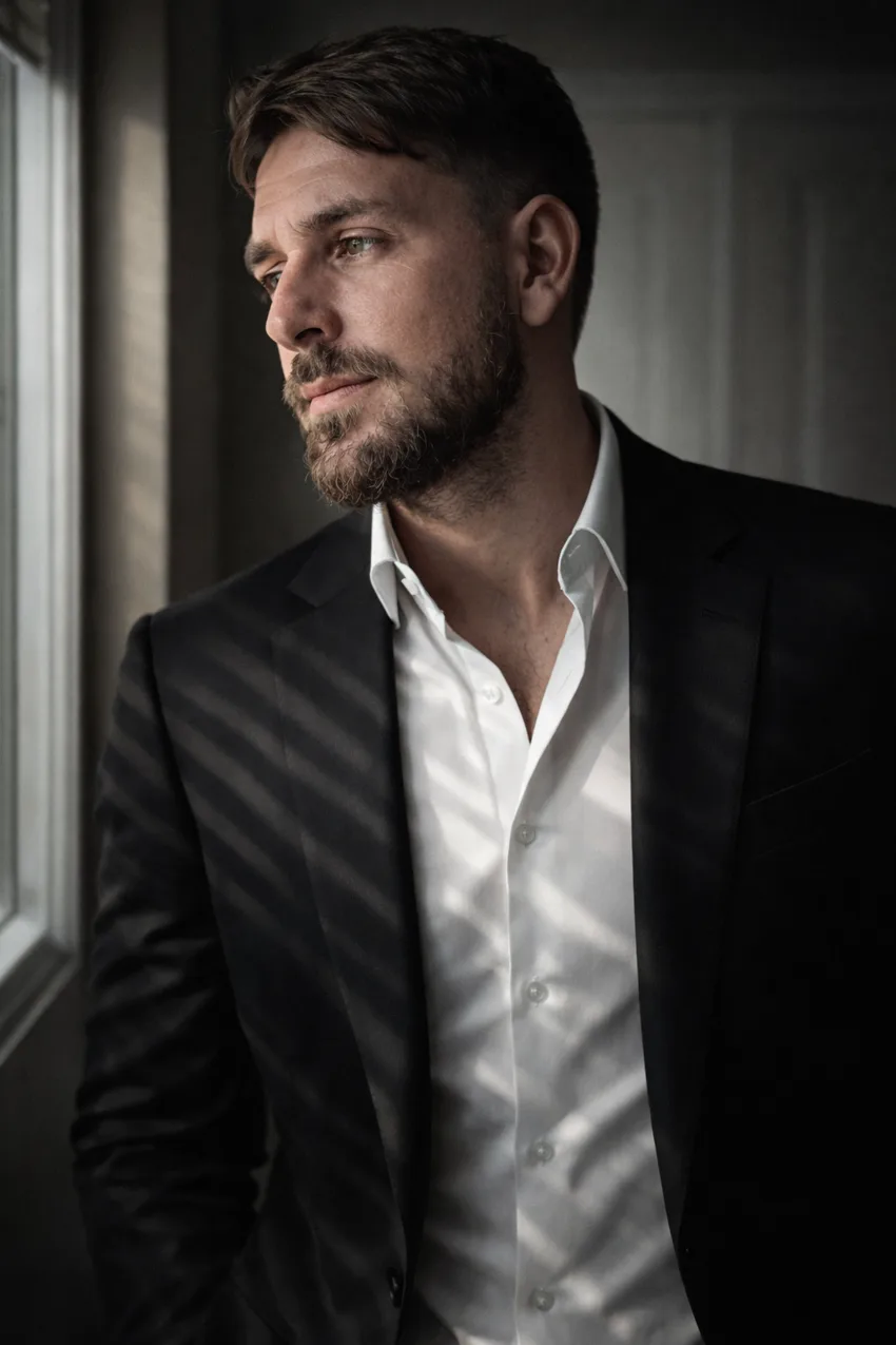 Kenneth in a black suit looking thoughtfully toward a window